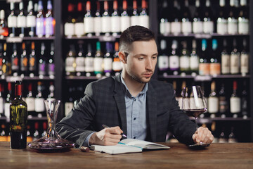 Sommeliers male hold glass red wine tasting and making notes degustation card