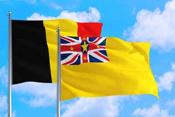 Niue and Belgium national flag waving in the windy deep blue sky. Diplomacy and international relations concept.