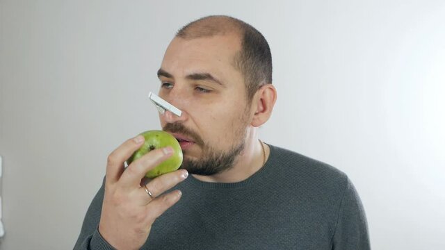 The man does not smell and taste, the sense of smell is lost, the symptoms of coronavirus. Man with a clothespin on his nose trying to smell the apple