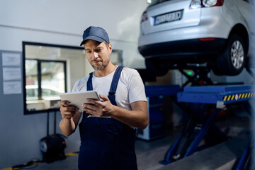 Smiling mechanic using digital tablet at auto repair shop.