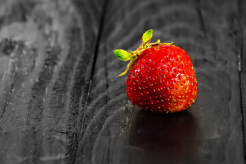 one strawberry on a black wooden background