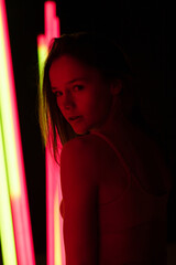 Sexy young woman with sensual lips posing in a photo studio on a dark background with neon lamps...