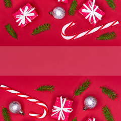 Christmas decorations layout or flatlay with fir branches, gifts, balls and candy canes on red background with copy space.