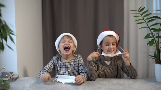 two little girls in santa hats take off medical mask. Christmas celebration on lockdown