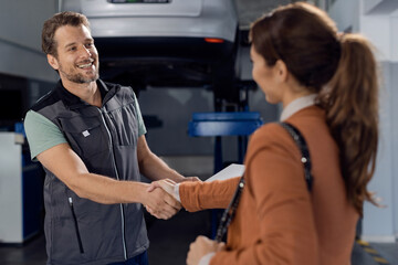 Happy auto repairman handshaking with female customer in a workshop.