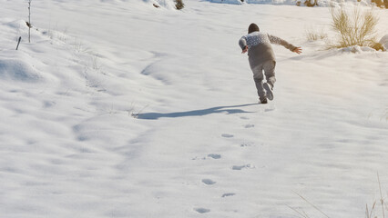 Naklejka na ściany i meble young boy running playing in the snow on a sunny day, happy with the cold