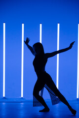 Silhouette of a attractive young woman dancer dancing in a room with neon lamps. Sporty beautiful girl model enjoys a dance in the studio with neon amazing color.