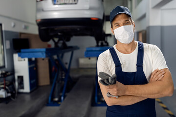 Fototapeta na wymiar Auto repairman standing with arms crossed while wearing face mask in a workshop.