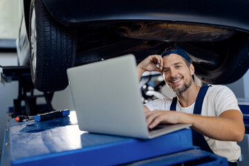 Happy repairman using computer while working at car workshop.