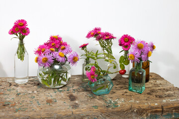 Autumn asters in small pharmacy bottles instead of vases on a long wooden bench