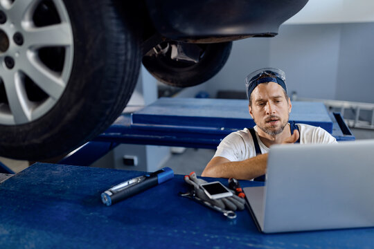 Car mechanic using laptop while working at auto repair shop.