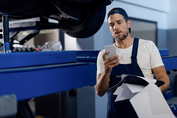 Auto mechanic texting on mobile phone while working at repair shop.