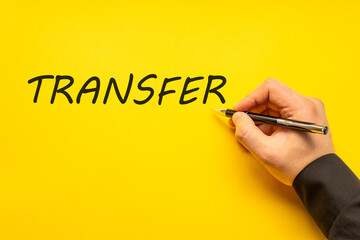 Male hand writes in black pen the word transfer on a yellow background with copy space. Business...