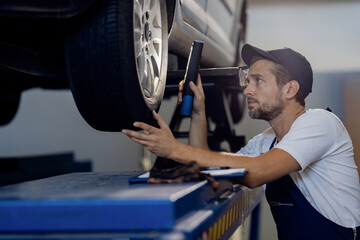 Auto repairman using flashlight while examining car tire in a workshop. - obrazy, fototapety, plakaty