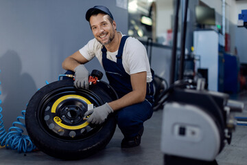 Fototapeta na wymiar Happy auto repairman checking pressure in a tire while working in repair shop.