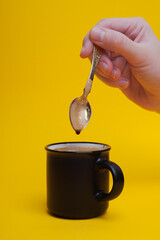 girl's hand stirring a spoon of coffee on a yellow background