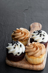 Set of mini cupcakes on wooden board on black stone background