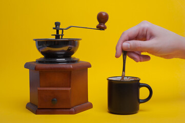 girl's hand stirring a spoon of coffee on a yellow background