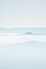 mystical and romantic bright scenery with layers of mountaintops softly peaking out of white clouds. Beautiful landscape with soft hills in a winter atmosphere lit by the setting sun