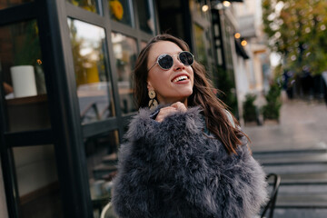 Obraz premium Pretty laughing girl has a good time in autumn weekend. Outdoor portrait of lovable trendy lady with brown hair wears stylish coat in autumn day.