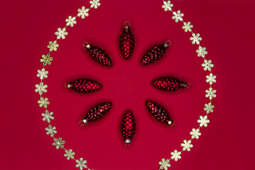 Christmas frame made of red cones and golden snowflakes garland on red background. Christmas decorations with copy space.