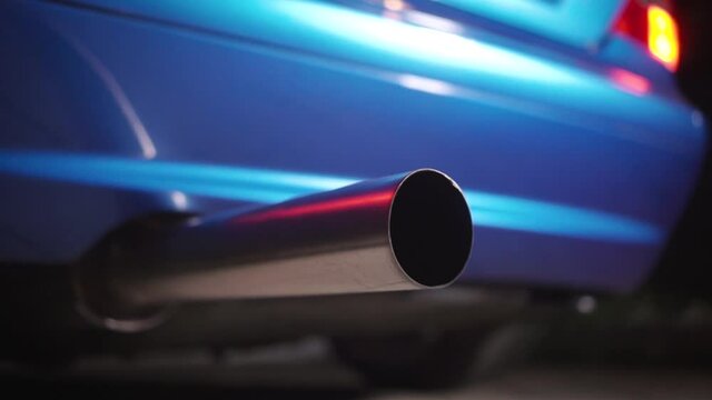 Close up of the exhaust pipe of a tuned sports car. Footage. Part symbol and conceptual tuning, motorsport, workshops, background. Vehicle standing on an asphalt road on a clear weather.