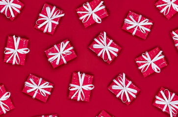 Pattern of gift boxes with white ribbons on a red background. Christmas flat lay.