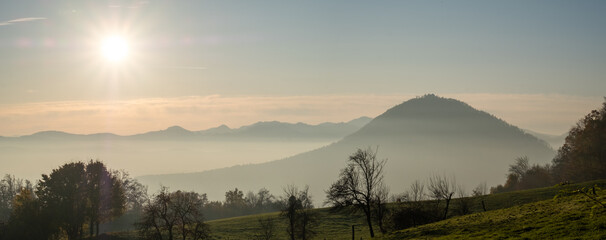 Obraz premium mountain view a beautiful landscape scenery with misty mountains and the setting sun in a blue and orange sky. Romantic scenery in a mountain hike