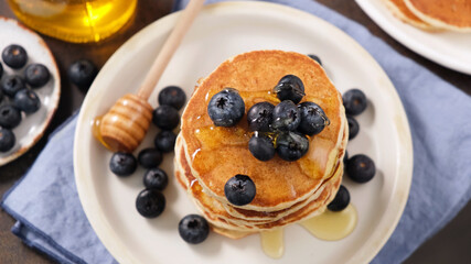 Pancakes with blueberries and honey on a plate, top view