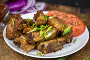 Grilled fat pork ribs on a bone served on a plate with vegetables. Roasted barbeque meat on dark background.