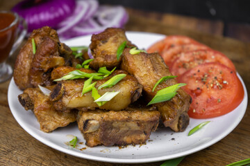 Grilled fat pork ribs on a bone served on a plate with vegetables. Roasted barbeque meat on dark background.