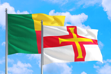 Guernsey and Benin national flag waving in the windy deep blue sky. Diplomacy and international relations concept.