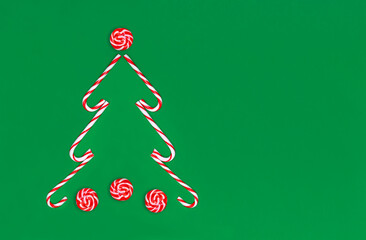 Christmas tree made of candy canes and striped red and white caramel on a green background with copy space
