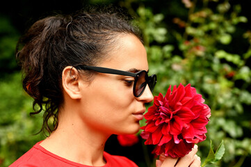 Beautiful young woman smelling red flower in the park.