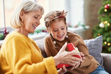 Happy family on Christmas morning. Affectionate grandmother and cheerful granddaughter open a...