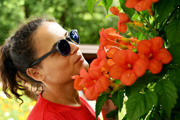 Beautiful young woman smelling red flowers in the park.
