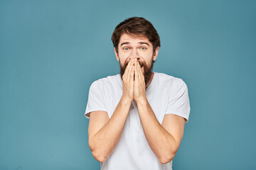 A bearded man in a white T-shirt gestures with his hands emotions blue background