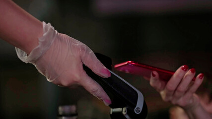 Human hand holding smartphone over payment terminal. waiter with rubber gloves