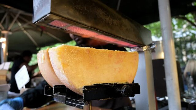 Melted cheese bubbling on a half wheel of cheese raclette under the glowing flames on a street food stall at Borough Market, London