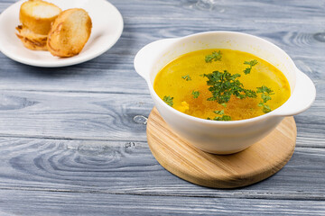 Chicken soup in a white plate with bread, on a wooden background