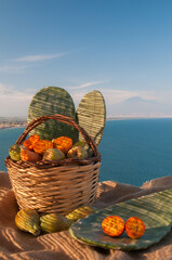 Prickly pears and a wicker baslet on a piece of jute, blue sea and Mount Etna in the background
