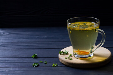 Chicken broth with herbs and carrots in glass, on wooden background
