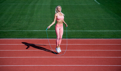 Obraz premium sexy lady in fitness sportswear. jumping on outdoor arena. training and workout. athletic female coach with skipping rope. woman sport trainer. healthy sporty lifestyle. health and energy