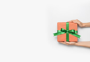 Female hands hold gift box in striped craft paper with green bow on light background flat lay top view copy space. Holiday present, christmas, new year, birthday, valentine's day, 8 march. Surprise