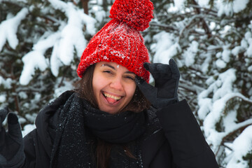 portrait of young smiling woman in winter clothes in red hat with bubo fir tree in background