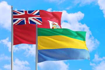 Gabon and Bermuda national flag waving in the windy deep blue sky. Diplomacy and international...