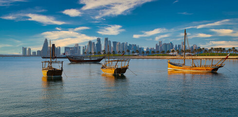 Doha skyline in Doha Qatar from the corniche promenade afternoon shot showing dhows with Qatar flag...