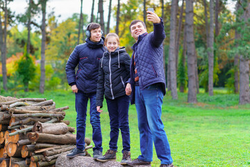 family relaxing outdoor in autumn city park, happy people together, parent and children, they standing on a log, playing, taking selfie by a phone
