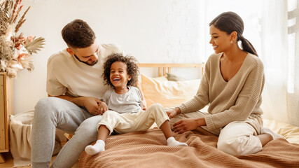 happy multi ethnic family mom, dad and child  laughing, playing and tickles   in bed   at home.