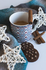 Obraz na płótnie Canvas A cup of coffee surrounded by cinnamon sticks, cookies, decoration, and a scarf. Blue morning composition.